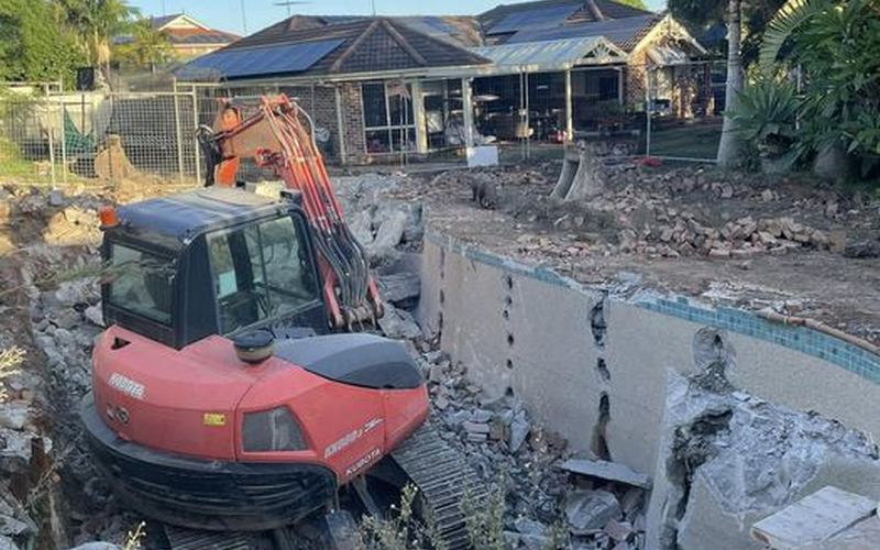 Pool demolition in progress Darwin — excavator breaking up concrete pool shell